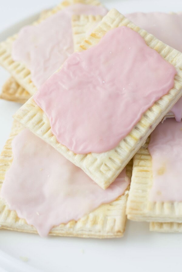 A stack of rectangular pastries with light pink icing on a white plate. The pastries have crumbly edges and a slightly toasted appearance.