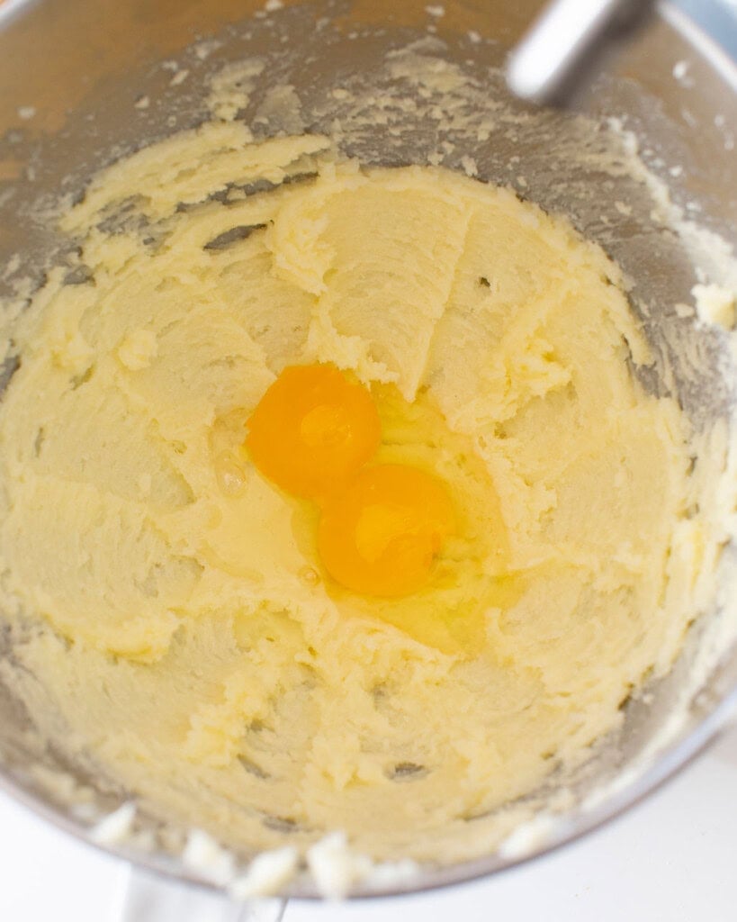 Butter and sugar mixture mixed with two raw eggs on top in a stand mixer bowl.