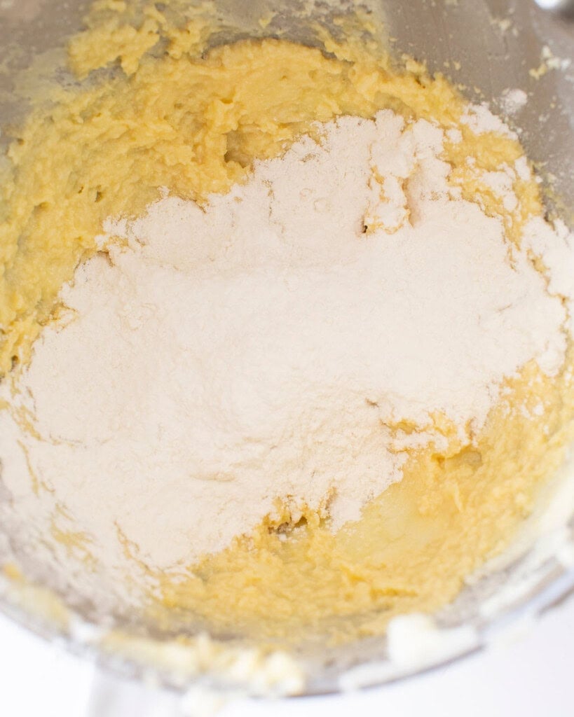 Butter, sugar, and egg mixture with flour on top in a stand mixer bowl.