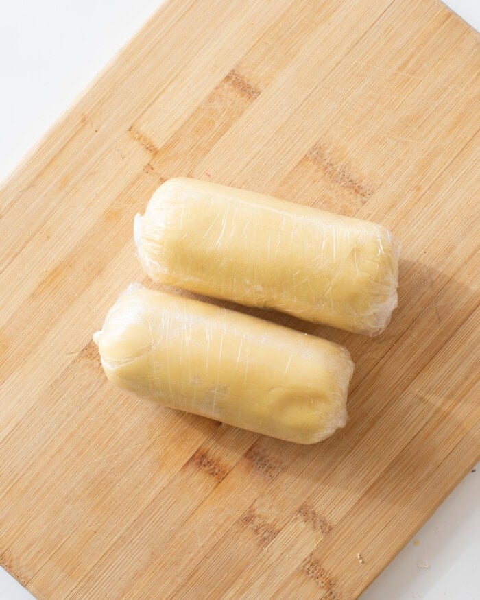 Sugar cookie dough wrapped in plastic wrap on a cutting board.
