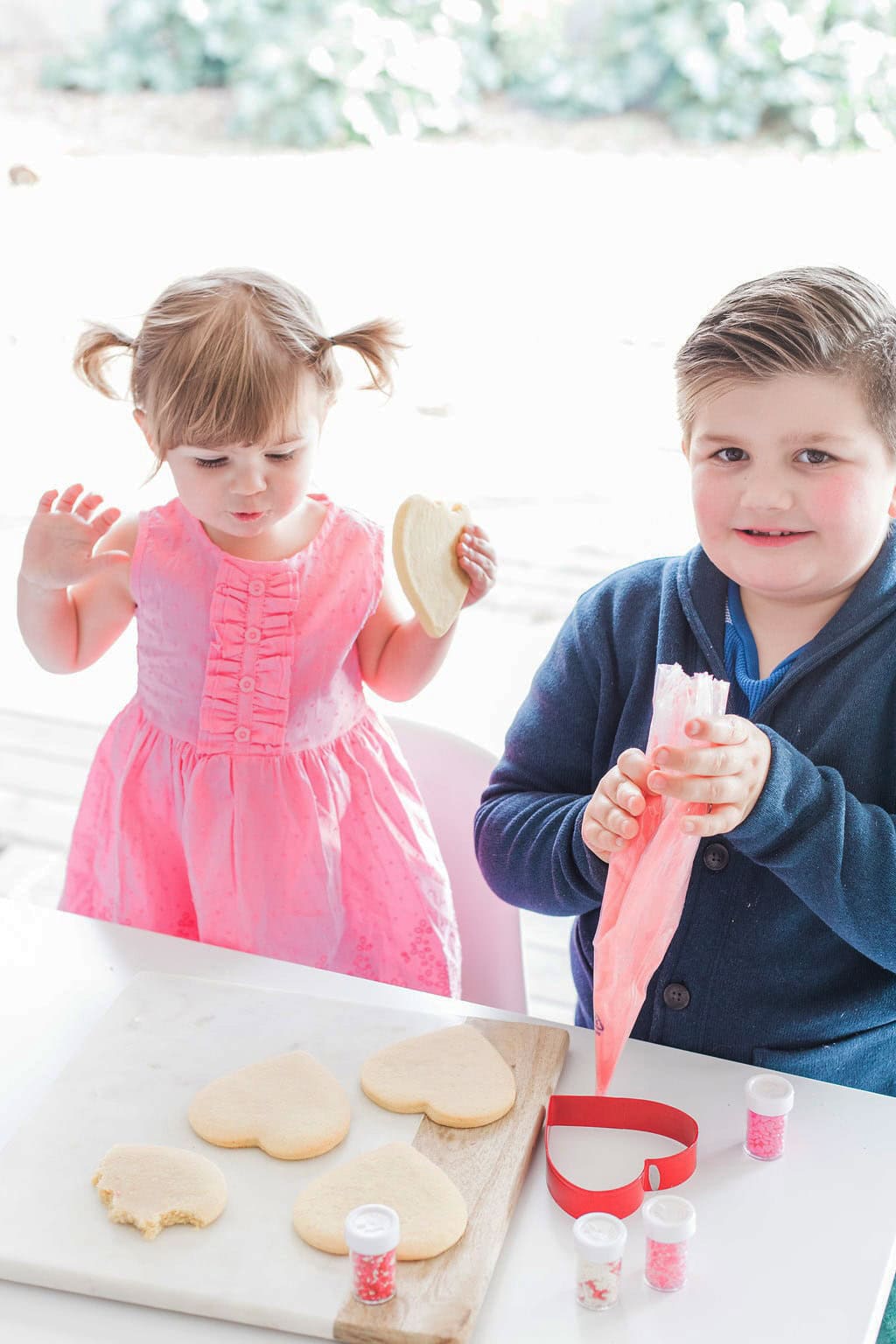 Two small children a girl, and a boy decorating heart shaped cookies. 
