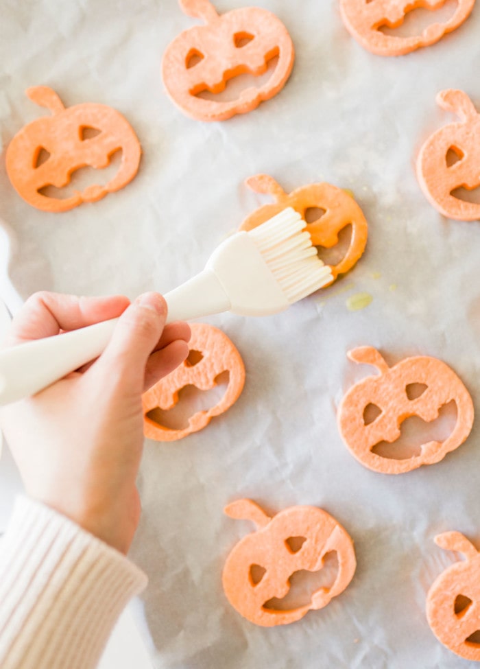 Brushing oil on sliced sweet potatoes for halloween snacks.