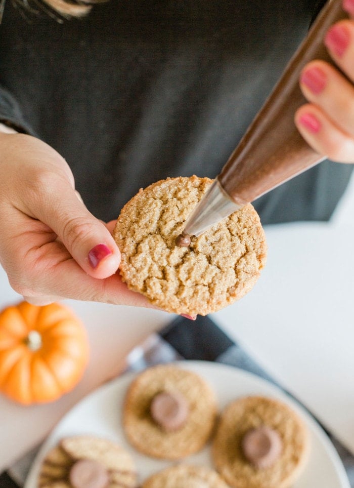 Piping chocolate frosting onto a peanut butter cookie to make Halloween Spider Cookies.