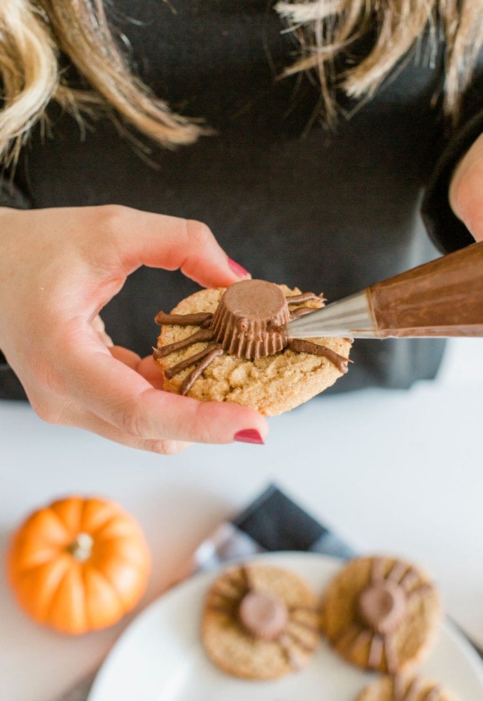 Adding chocolate frosting dots to attach candy eyes to Halloween Cookies.
