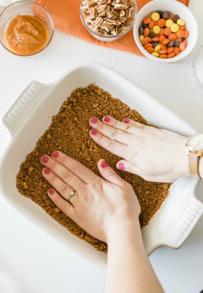 Pressing the crushed ginger snap mixture firmly into the baking pan for the Pumpkin Magic Bars.