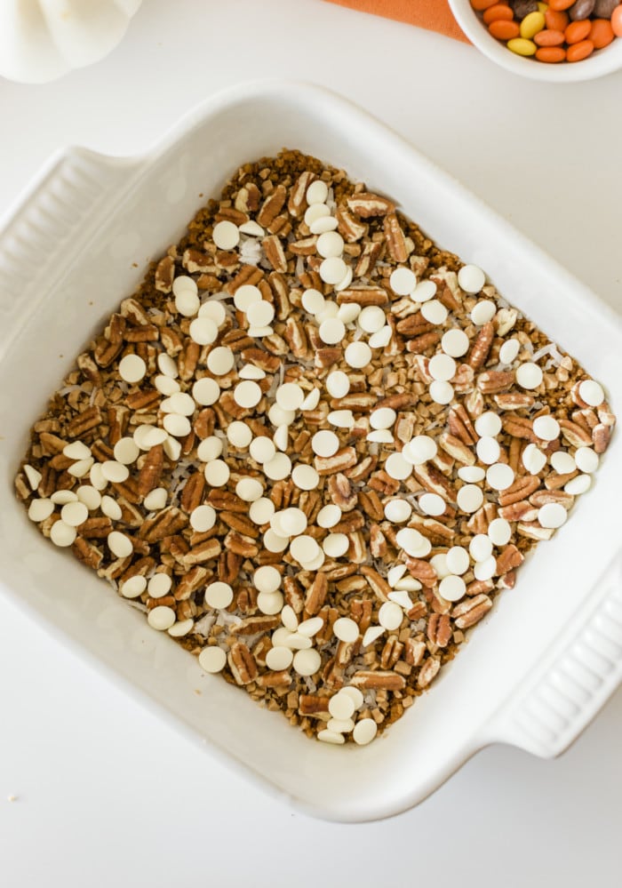 Pumpkin magic bars in a baking dish topped with pecans and white chocolate chips.