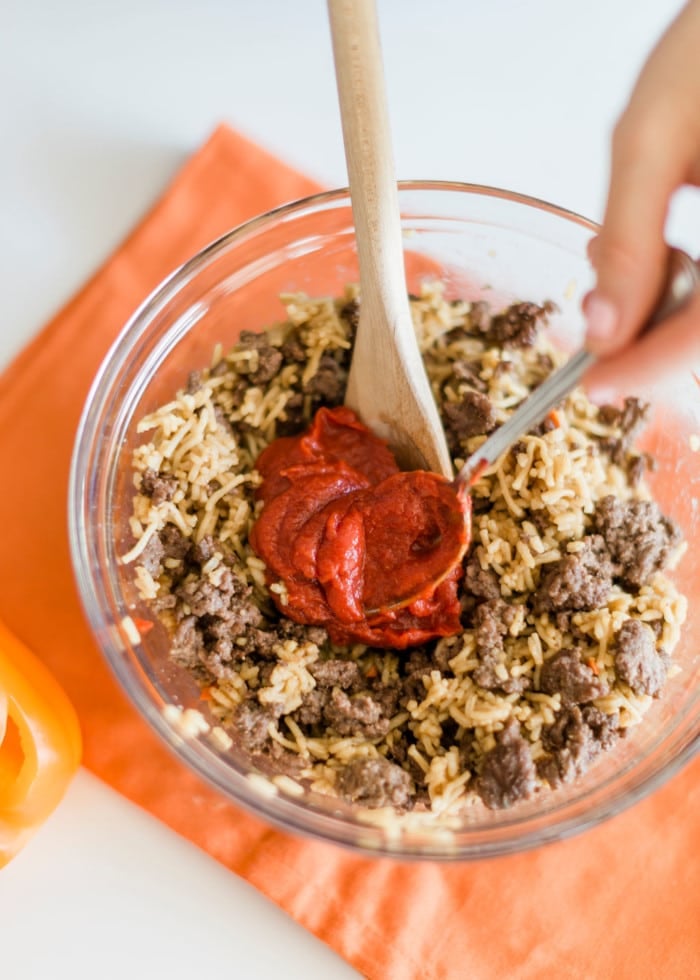 mixing tomato paste and rice in a bowl for stuffed bell peppers.
