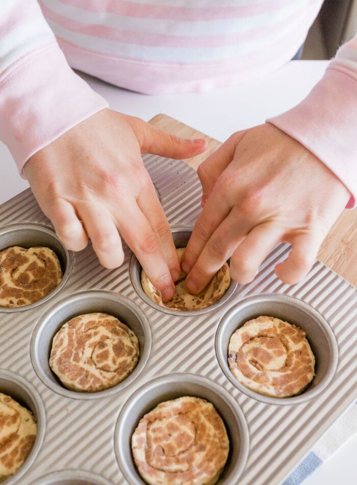 Cinnamon roll apple pie dough being pressed into a muffin tin.