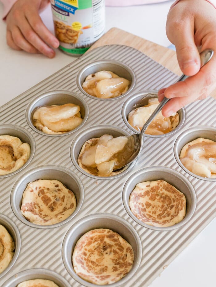 Cinnamon roll apple pie cups filled with apple pie filling in a muffin tin.