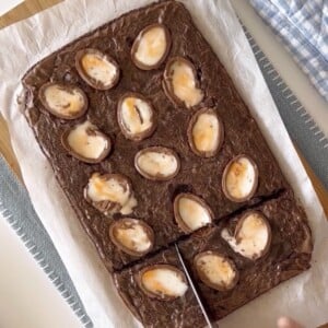 Slicing with a knife baked cadbruy egg brownies on a wood cutting board.