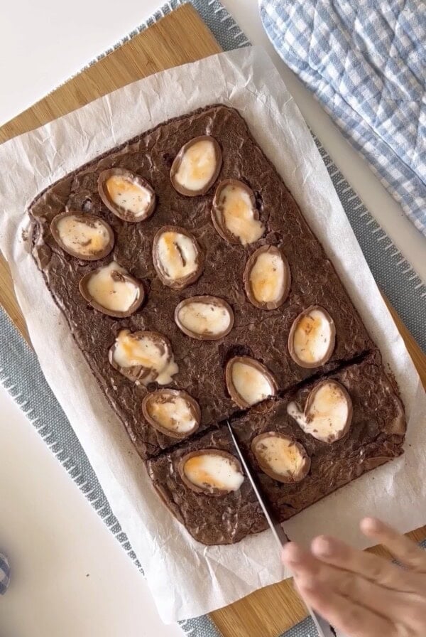 Slicing with a knife baked cadbruy egg brownies on a wood cutting board.