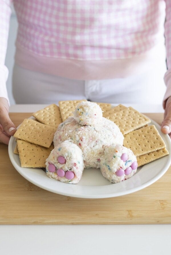 Easter dessert shaped into a bunny butt displayed on white plate surrounded by graham crackers on wood cutting board.