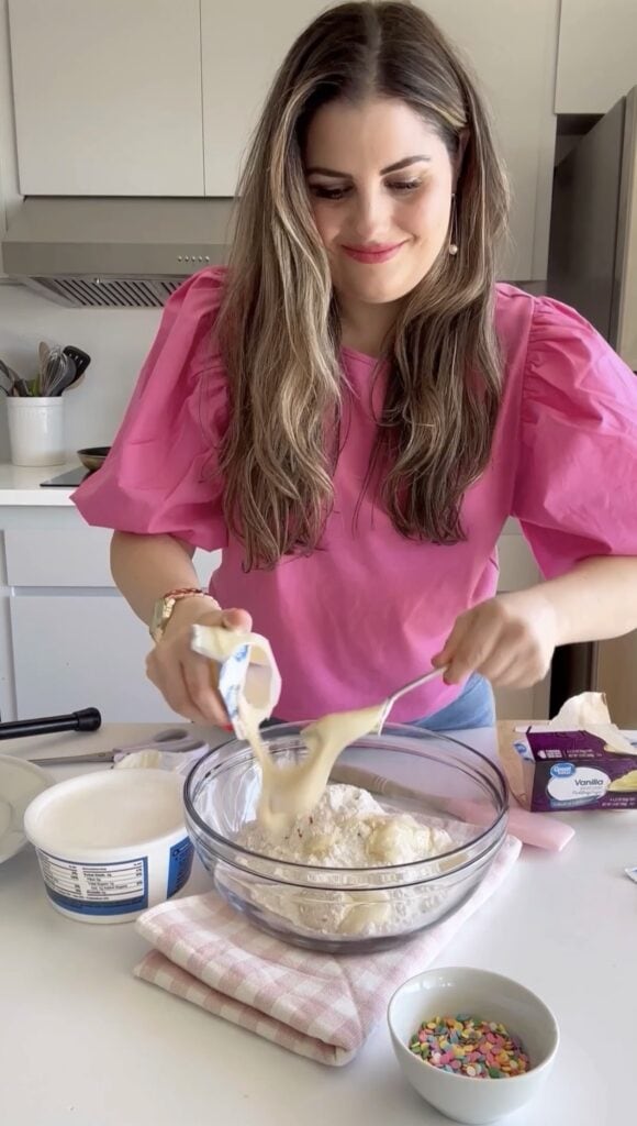 Adding pudding to funfetti dip recipe in a clear bowl.