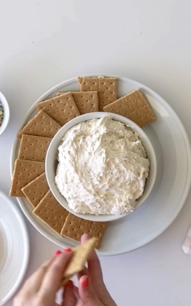 Funfetti dip in white bowl placed on top of another white bowl with graham crackers displayed around it.