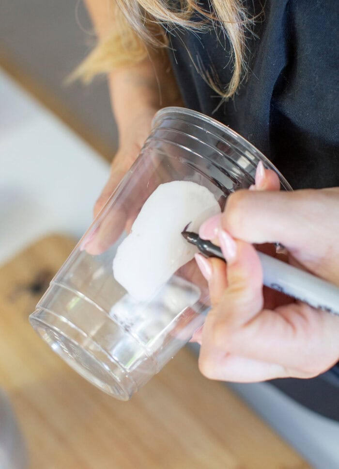 Person writing a ghost face on a clear cup for Halloween drinks.