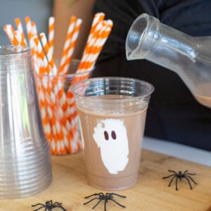 Person pouring chocolate milk into a ghost cup for Halloween drinks.