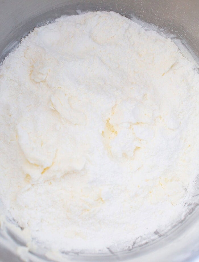 Powdered sugar added for a buttercream frosting recipe in a mixing bowl.