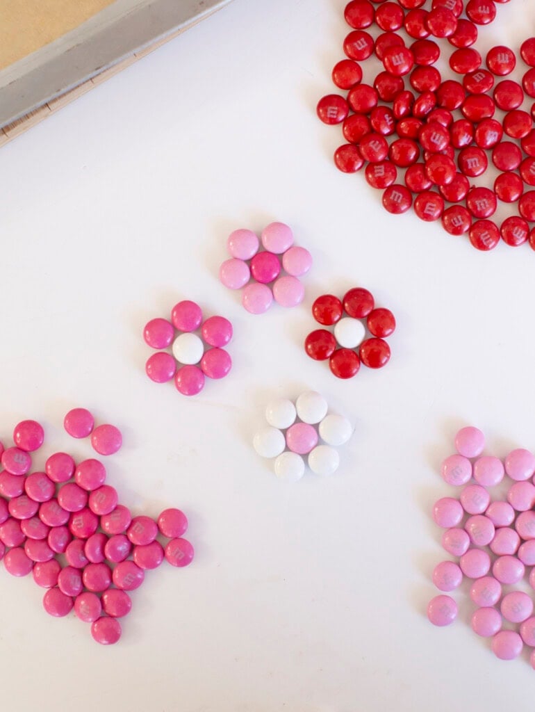  M&Ms arranged as flowers on parchment, ready for pretzels.