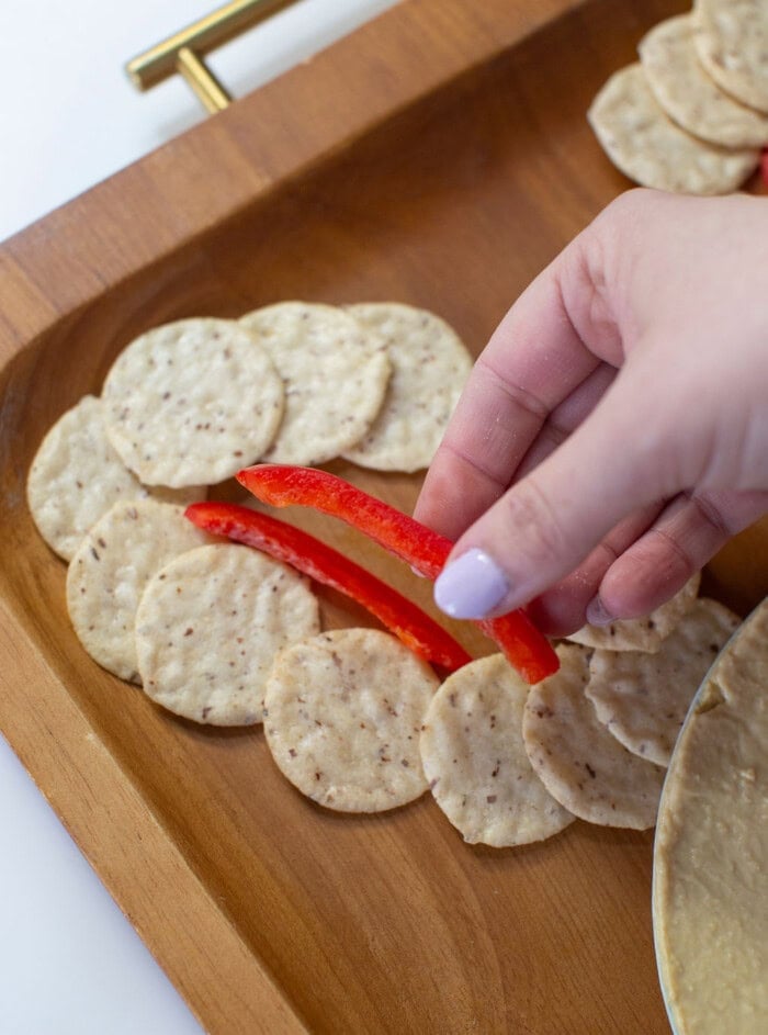 hand adding red bell peppers between crackers that are shaped like a bunny ear.