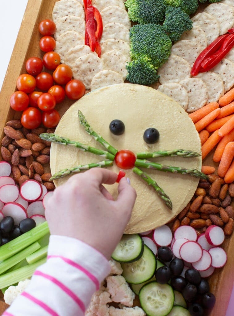 Close up shot of veggie tray that shows a hand putting red bell pepper on mouth of Easter bunny