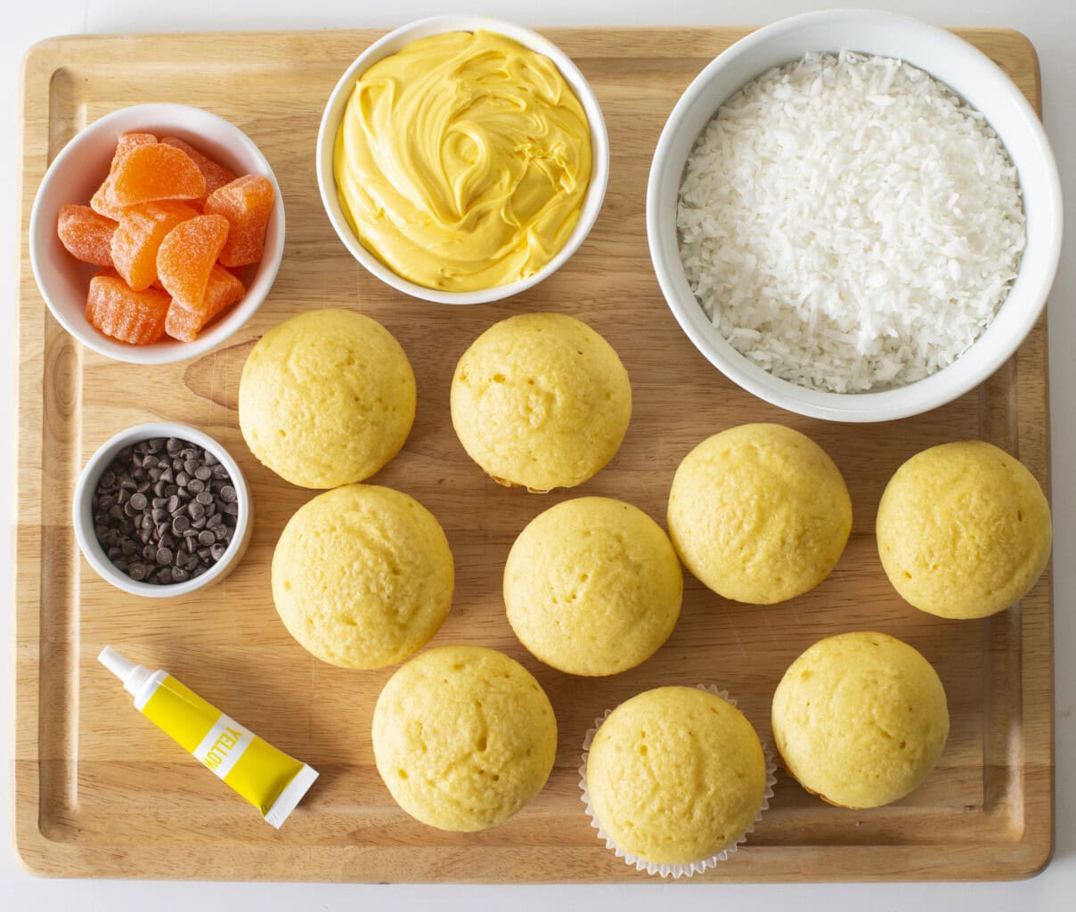 Ingredient shot on a wooden cutting board of all of the ingredients needed to make Easter Chick cupcakes.