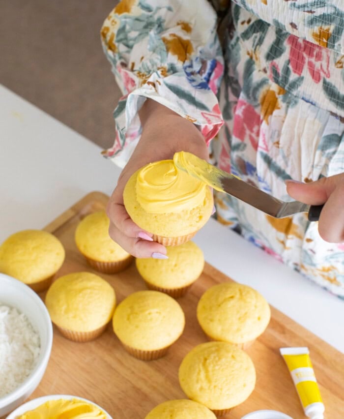 Frosting cupcakes with yellow frosting.