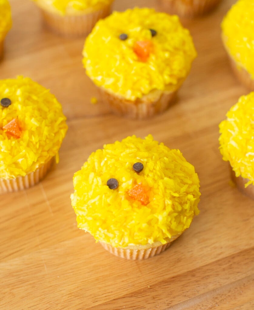 Easter chick cupcakes on a wooden cutting board.
