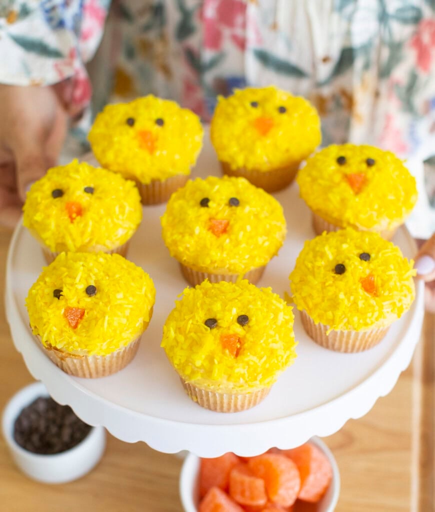 Yellow Easter chick cupcakes on a white cake stand.