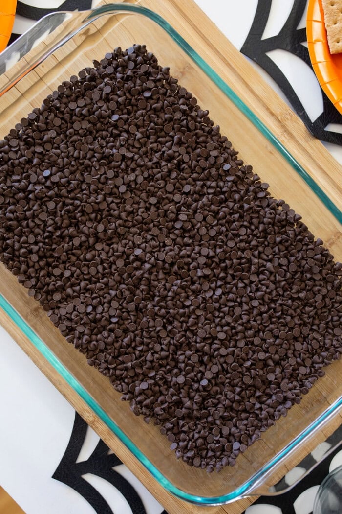 Adding chocolate chips to a 9x13 baking dish for the s’mores dip.