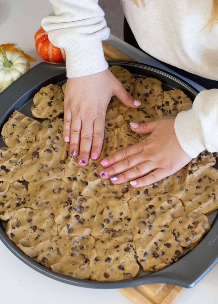 Pressing cookie dough into an even layer in the bottom of round baking pan.