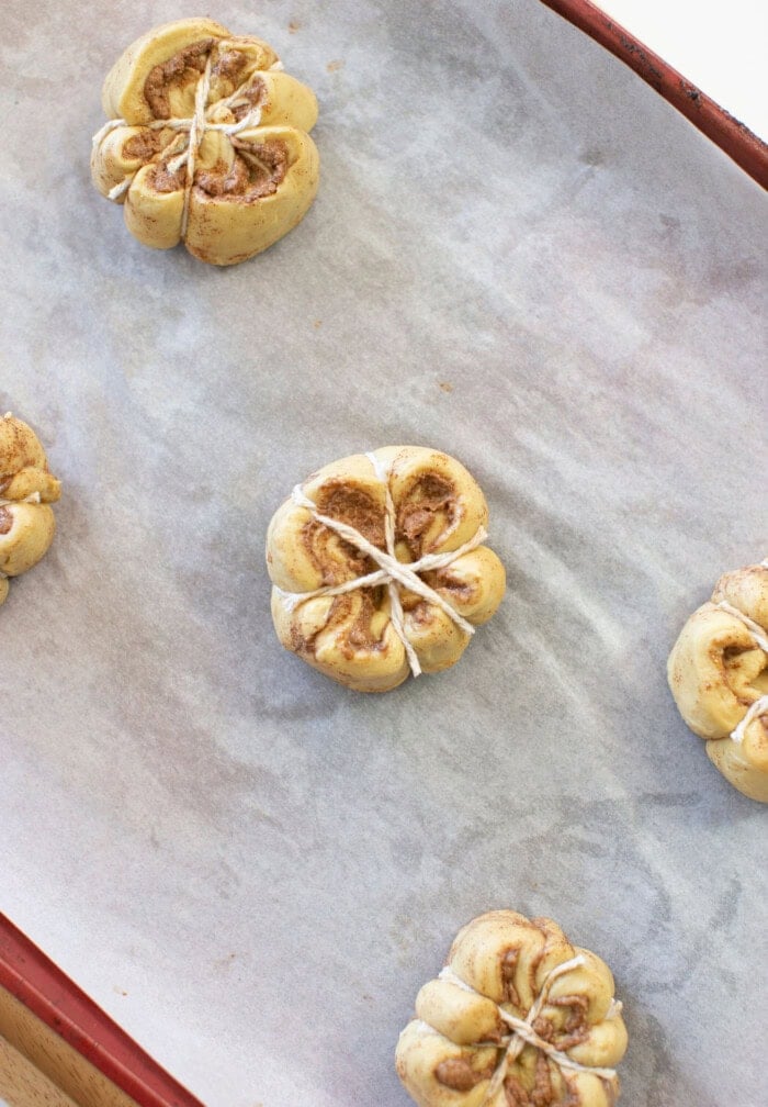 Pumpkin cinnamon roll tied with kitchen twine to create a pumpkin shape.