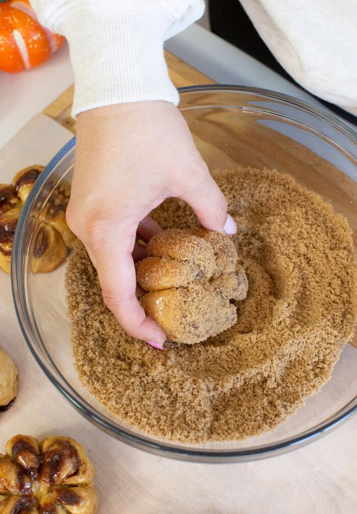 Dipping pumpkin cinnamon rolls into cinnamon sugar in a bowl.