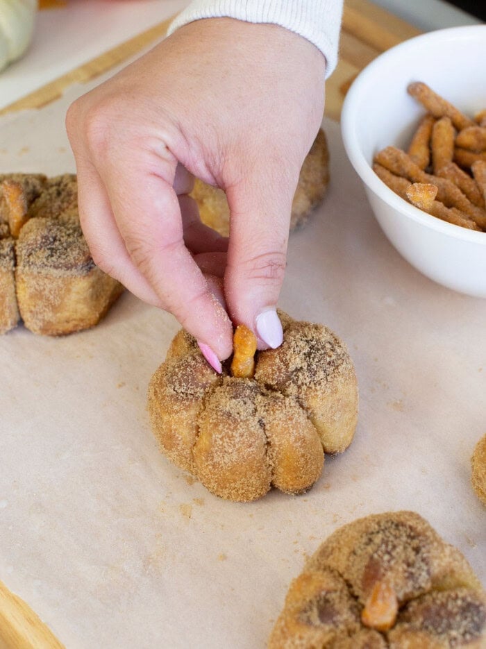 Adding pretzel to the center of pumpkin cinnamon rolls to create the stems.