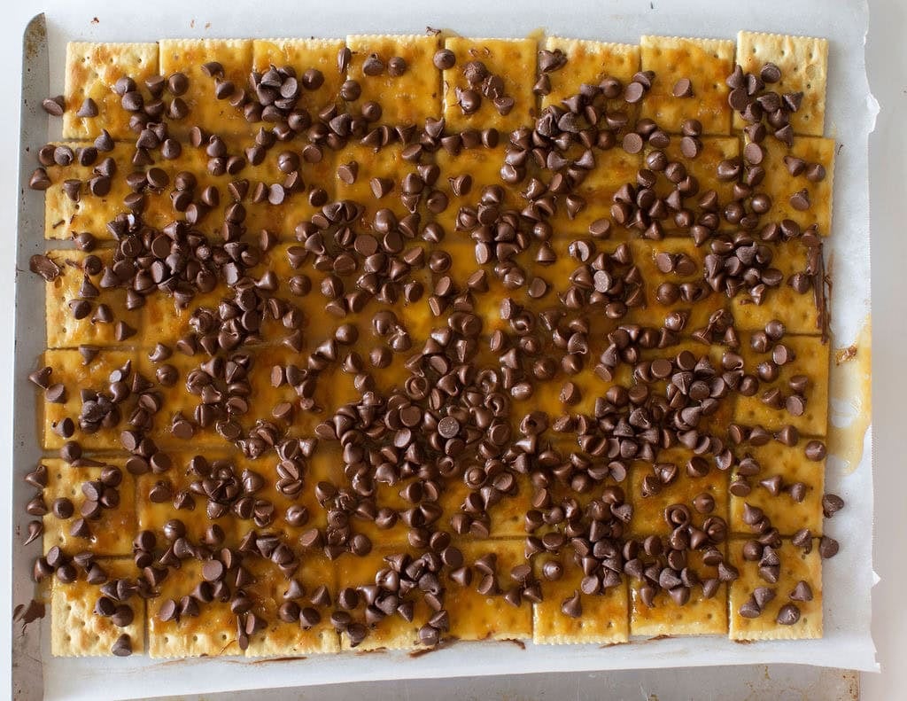 A baking tray filled with crackers topped with a layer of caramel and sprinkled with chocolate chips.