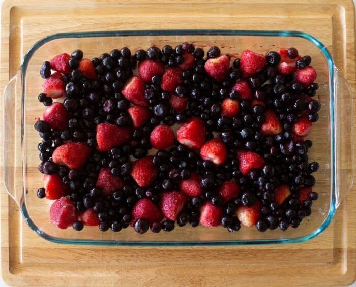A glass baking dish filled with a mix of strawberries and blueberries, placed on a wooden surface. The fruit is vibrant and evenly spread across the dish.