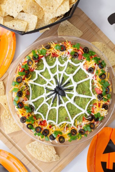A Halloween bean dip with a sour cream spider web, fresh toppings, and tortilla chips.