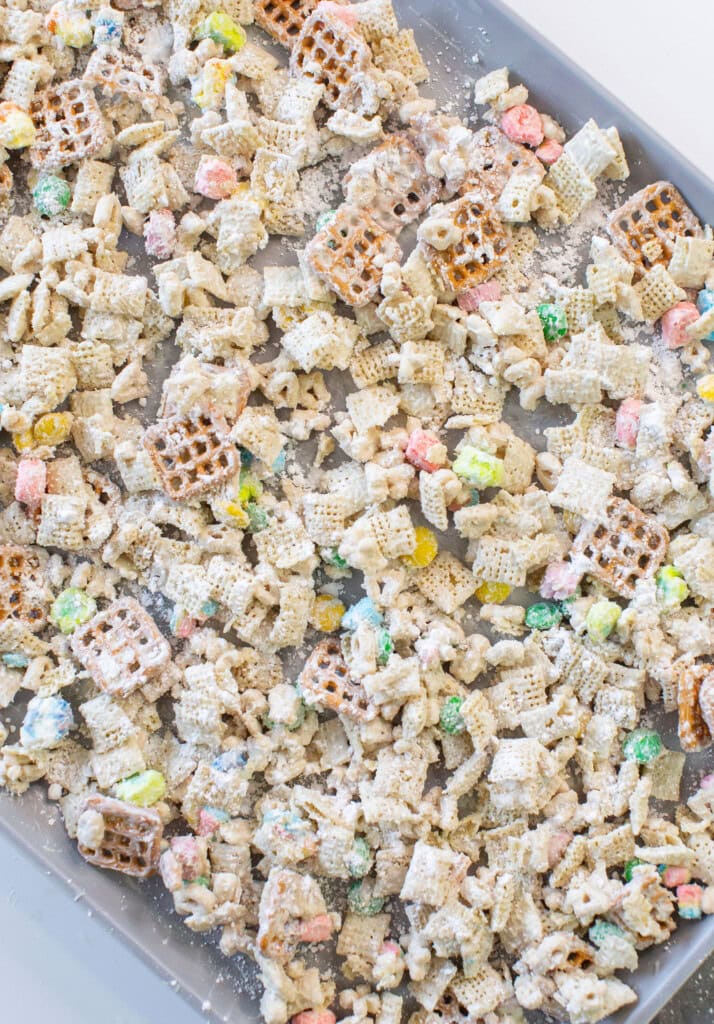 A baking sheet filled with a colorful snack mix of pretzels, Chex cereal, mini marshmallows, coated in a white powdered coating, likely powdered sugar.