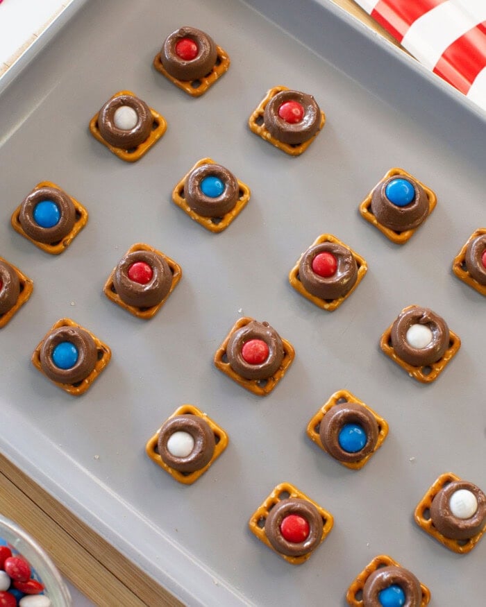 A baking tray with pretzel squares topped with melted chocolate and red, white, or blue candies, arranged in neat rows for a patriotic snack.